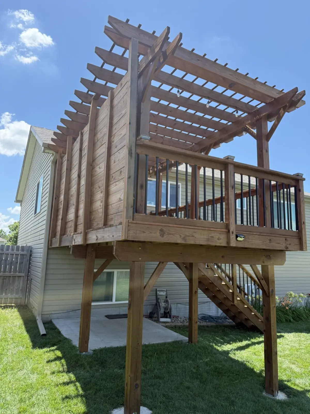 Stained wood deck with pergola, railings and stairs in a backyard